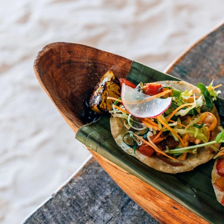 A seafood tostada with radish and carrot, served on a banana leaf